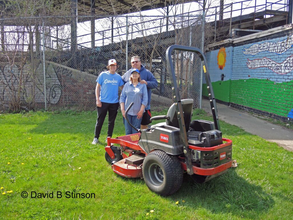 Three people next to a lawn mowing machine